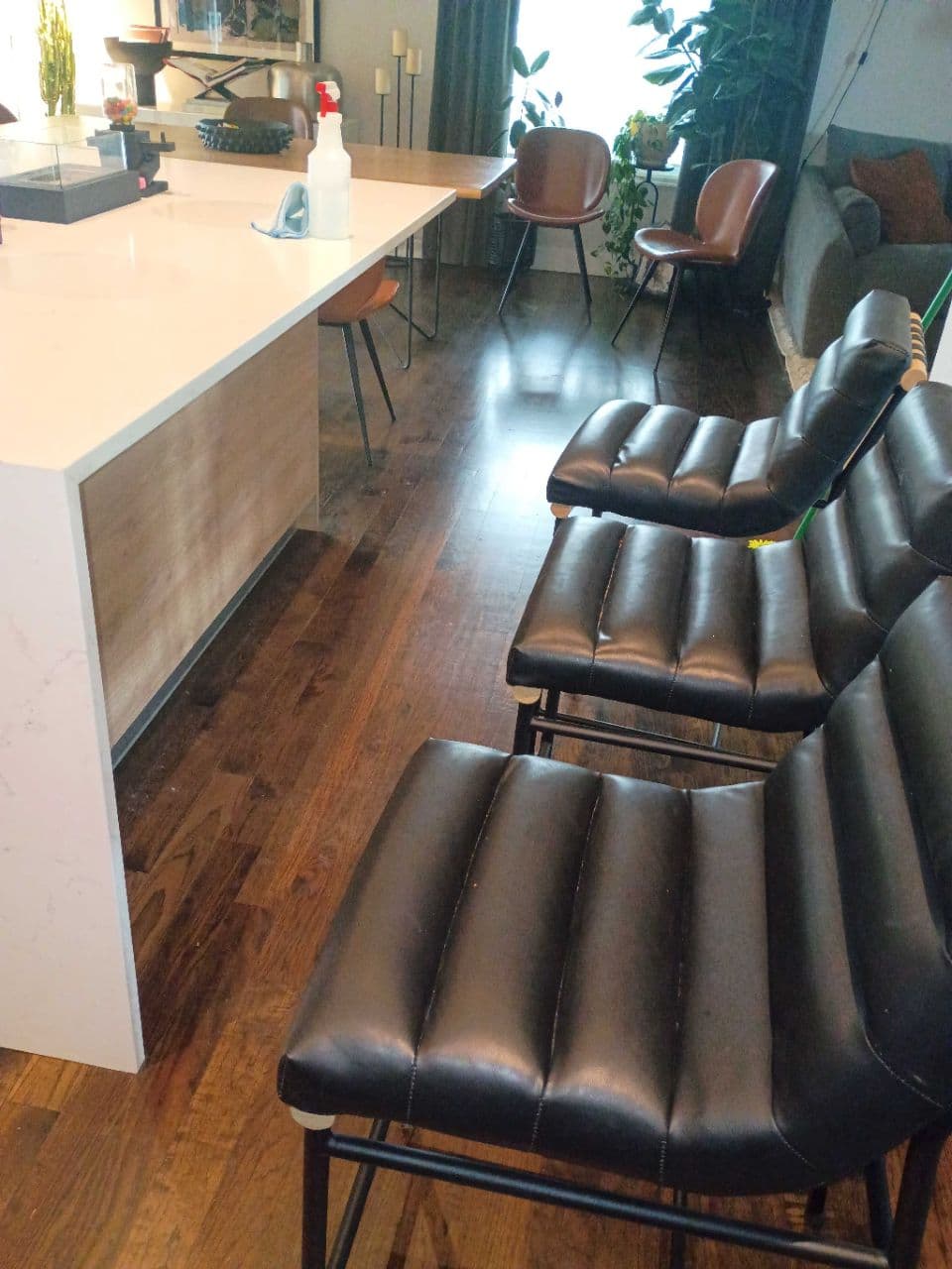 Three black ribbed leather bar stools lined up against a white and wood kitchen island.