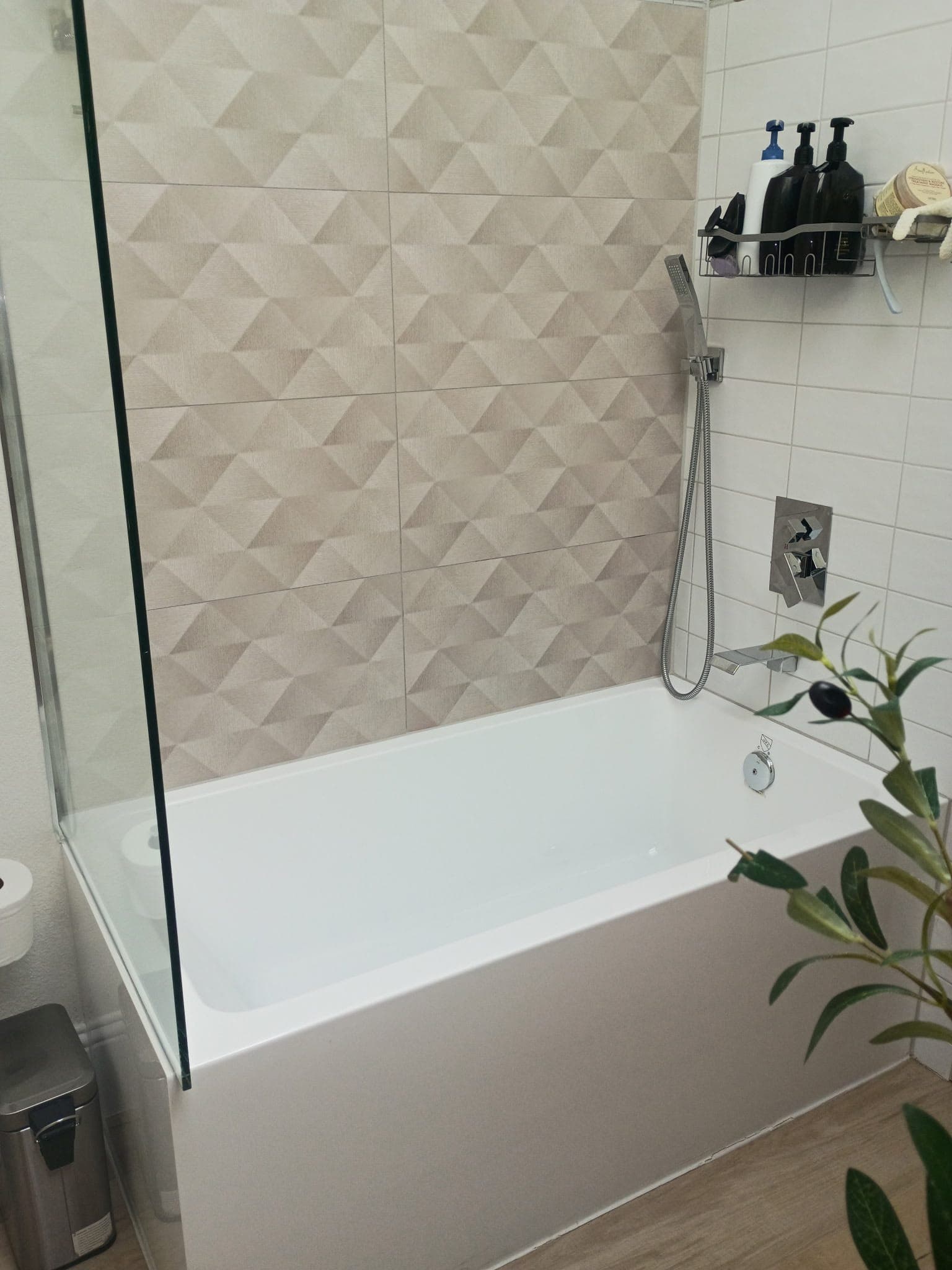 White bathtub with a glass screen and a textured beige geometric tile accent wall.