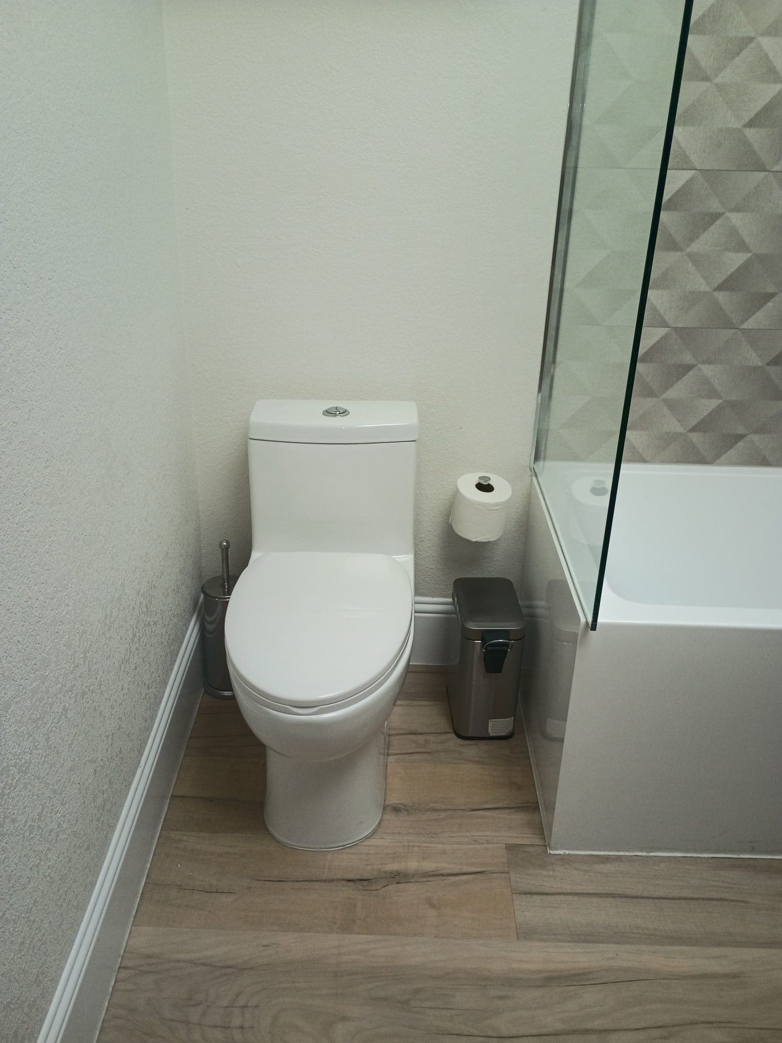 White toilet on wood-look flooring next to a bathtub with a glass partition.